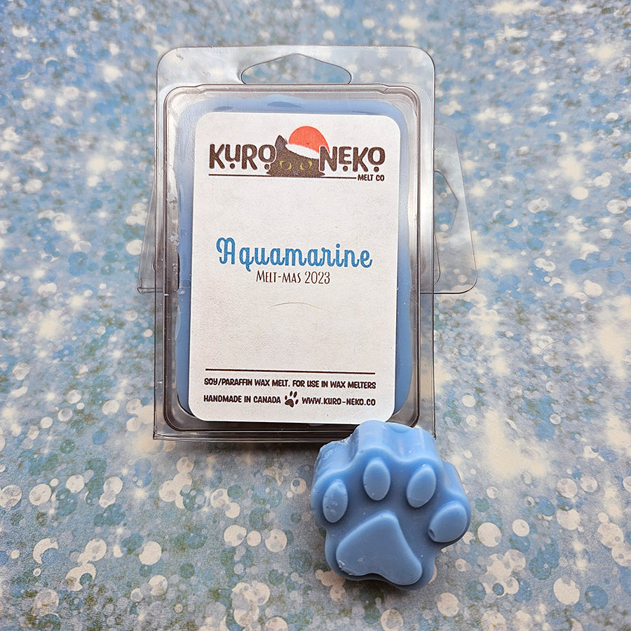 A set of wax melts in a clamshell on a blue speckled background with a paw shaped wax melt in front of it. The pictured scent is Aquamarine.