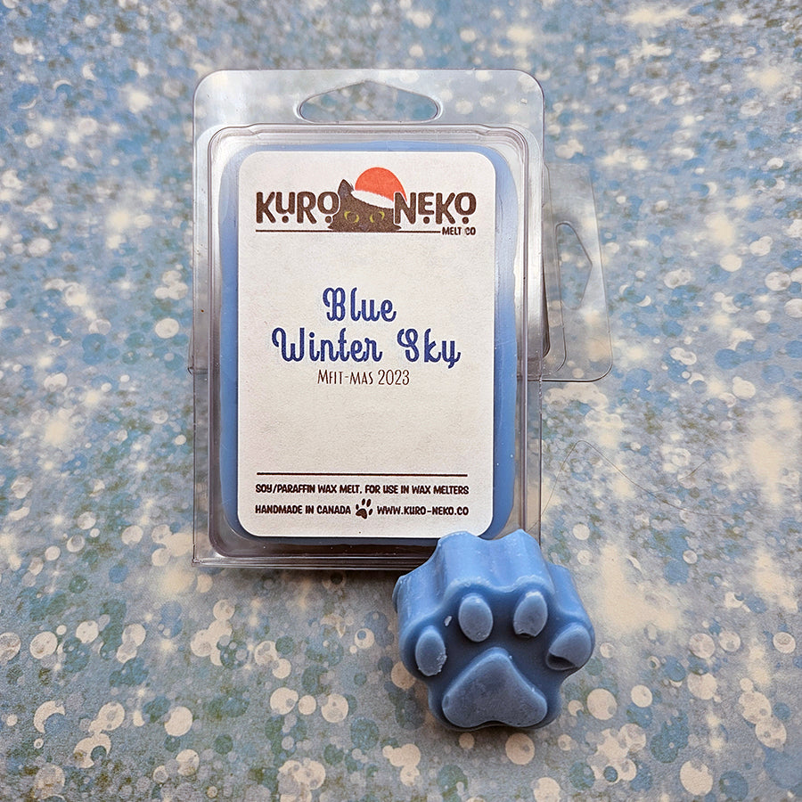 A set of wax melts in a clamshell on a blue speckled background with a paw shaped wax melt in front of it. The pictured scent is Blue Winter Sky.