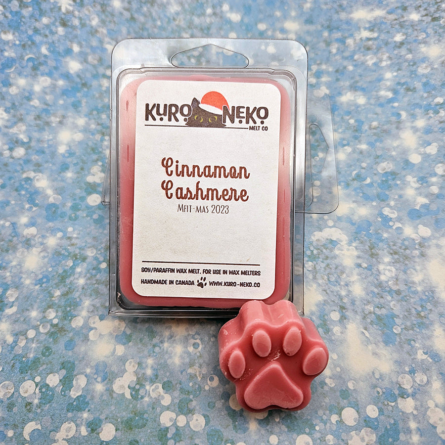 A set of wax melts in a clamshell on a blue speckled background with a paw shaped wax melt in front of it. The pictured scent is Cinnamon Cashmere.