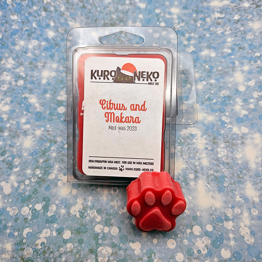 A set of wax melts in a clamshell on a blue speckled background with a paw shaped wax melt in front of it. The pictured scent is Citrus and Mokara.