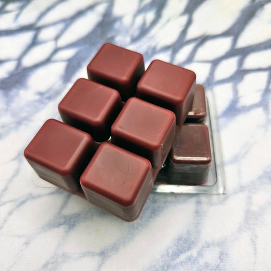 A set of wax melts in a clamshell on a dark blue and white tie dye background. The pictured scent is Adventure Calls: G'raha Tia.