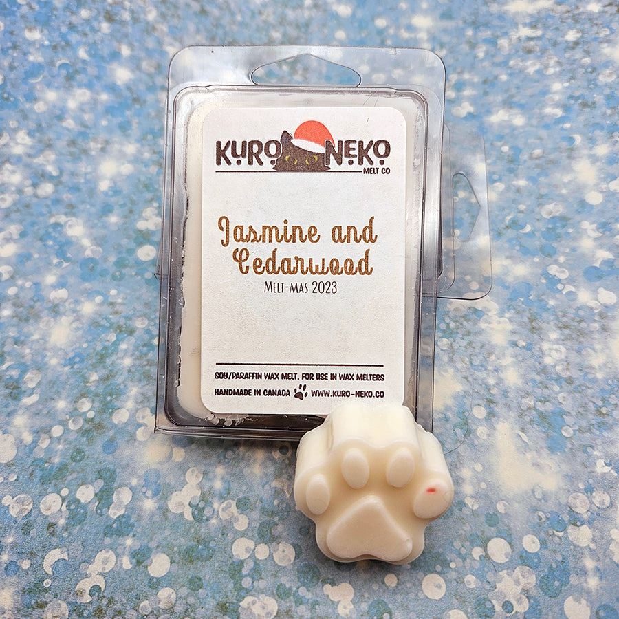 A set of wax melts in a clamshell on a blue speckled background with a paw shaped wax melt in front of it. The pictured scent is Jasmine and Cedarwood.