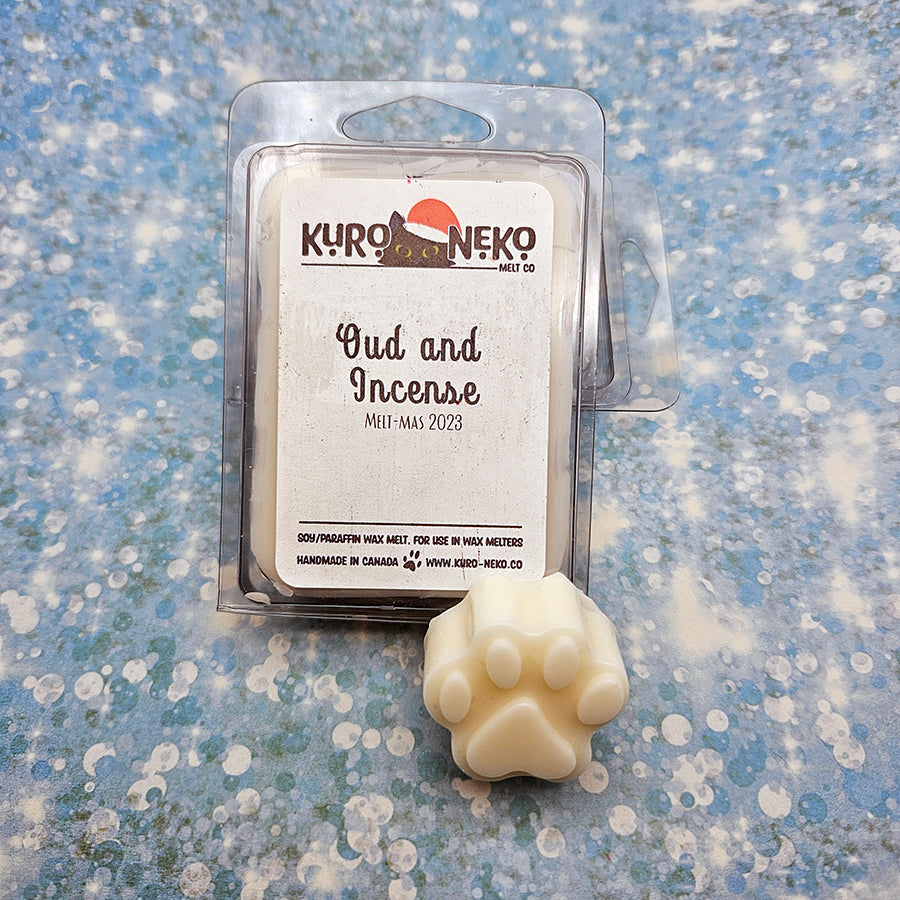 A set of wax melts in a clamshell on a blue speckled background with a paw shaped wax melt in front of it. The pictured scent is Oud and Incense.