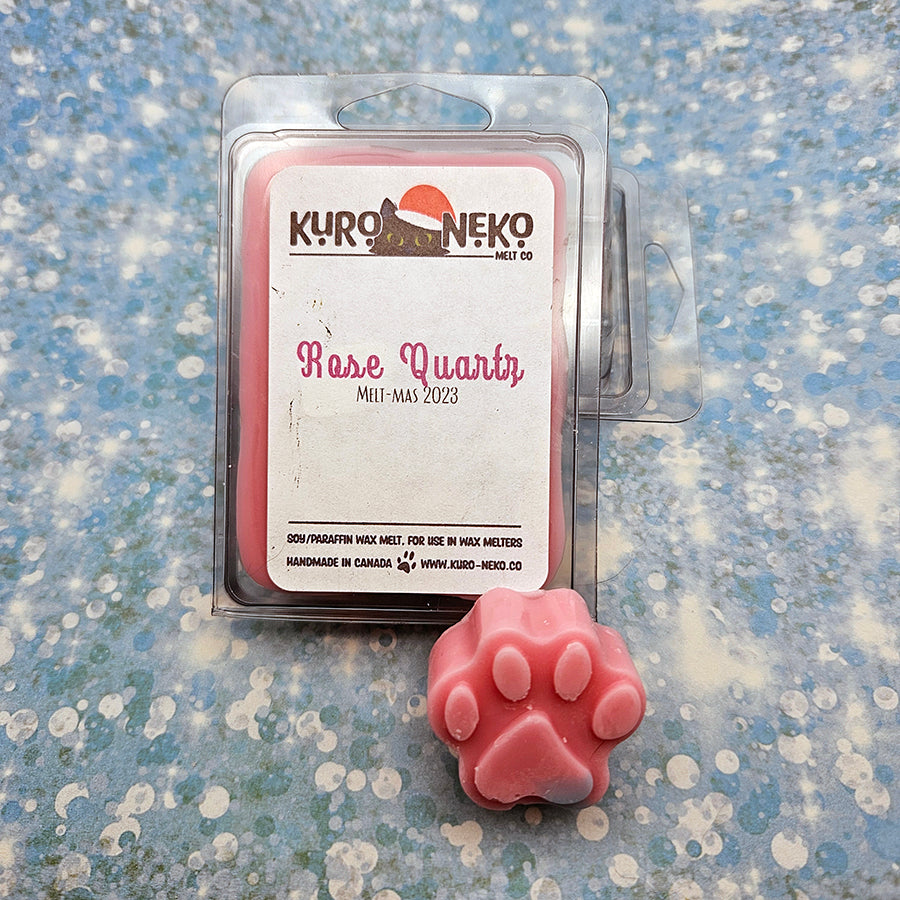 A set of wax melts in a clamshell on a blue speckled background with a paw shaped wax melt in front of it. The pictured scent is Rose Quartz.